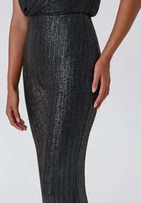 Jumpsuit nero metallico a coste con silhouette aderente, caratterizzato da un tessuto testurizzato e dettagli luccicanti, che mette in risalto la forma del corpo.