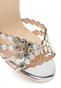 Zilveren sandaal met open teen en dubbele riemen, versierd met ronde iriserende stenen en golvende randen aan de binnenzool en riemen.