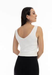 Top scurt tricotat alb cu un design în V la spate, având bretele groase și o textură în dungi. Asortat cu o fustă neagră pentru contrast.