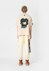 Camiseta oversized crema con un estampado gráfico en la parte trasera, combinada con pantalones amarillos pálidos y botas de tobillo marrones. Presenta un diseño sencillo.