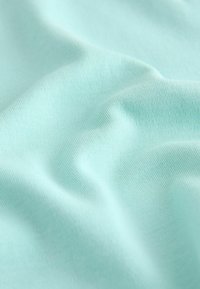 Tessuto azzurro chiaro con una trama fine a maglia, mostrato con pieghe morbide e ombre delicate che evidenziano la superficie liscia del materiale.