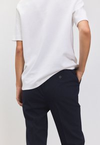 T-shirt blanc en coton avec un ourlet arrondi, associé à un pantalon bleu marine avec un détail de bouton visible à la taille et une poche.