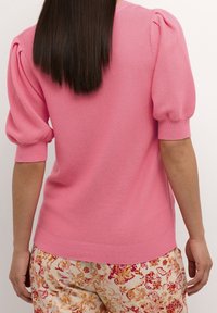 Korte roze pullover met pofmouwen, geribbelde details bij de manchetten en zoom, gecombineerd met broek met bloemenpatroon in zachte kleuren.