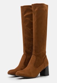 Bruna suède knähöga stövlar med klack, med en slät yta, spetsig tå och sidodragkedjor för enkel på- och avtagning.