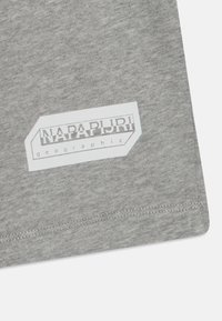 Šedá bavlněná tkanina s texturovaným povrchem, na které je umístěno bílé obdélníkové logo s nápisem "NAPAPIJRI geographic" blízko spodního lemu.