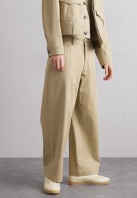 Beige skräddarsydd jacka med matchande vida byxor, med en texturerad tyg, framfickor och en avslappnad passform. Vita skor fulländar looken.