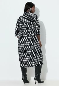 Długa sukienka w czarno-biały wzór, z rękawami o długości do łokcia, z geometrycznym nadrukiem i zwiewną sylwetką. Połączona z czarnymi kozakami za kolano.