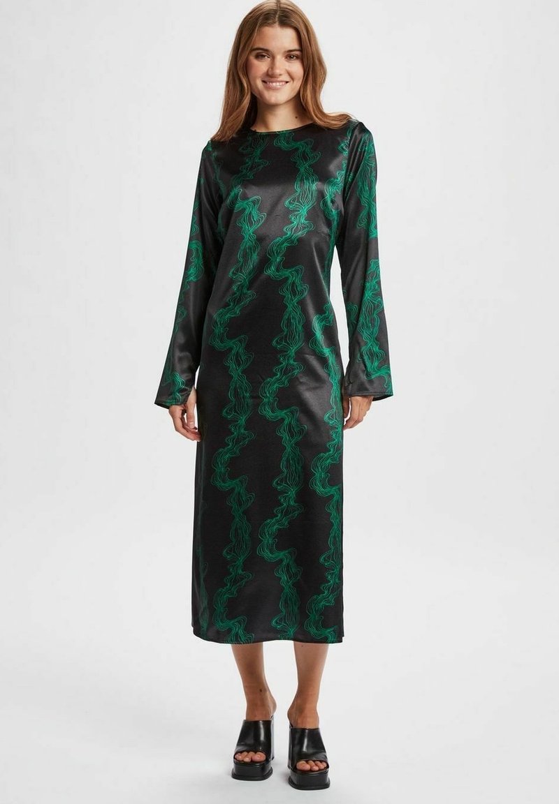 Rochie din satin negru cu mâneci lungi, având un model ondulat verde. Rochia are o croială dreaptă, reaching până la jumătatea gambei, și pantofi cu toc înalt negri.