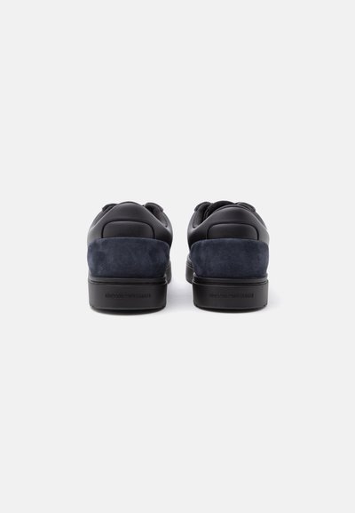 Paire de baskets basses noires et bleu foncé vues de dos sur fond blanc avec un marquage en relief sur les talons.