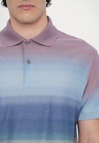 Homme portant un polo à manches courtes avec des rayures dégradées dans des tons de violet, bleu et gris clair, boutonné au col.