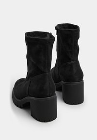 Czarne zamszowe botki za kostkę z masywną gumową podeszwą i słupkowym obcasem. Zamek błyskawiczny po boku ułatwia zakładanie.