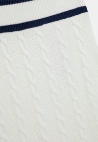 Tissu en tricot blanc avec une taille côtelée bleu marine profonde ; présente un motif texturé de tresses surélevées et des détails de points intriqués.