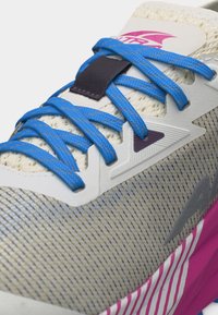 Κοντινή λήψη αθλητικού παπουτσιού με μπλε κορδόνια, γκρι επάνω μέρος από δίχτυ, ρόζ και λευκή σχεδιασμένη σόλα και μοβ λεπτομέρειες στο λογότυπο.