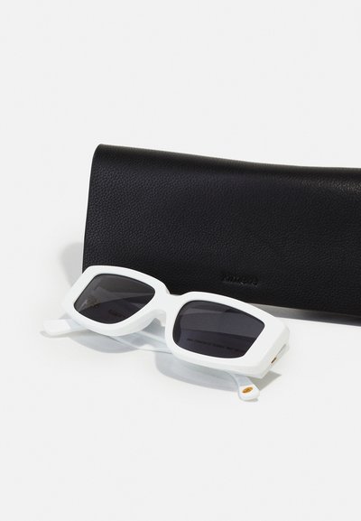Weiße Sonnenbrille mit einem dicken, eckigen Rahmen und dunklen Gläsern, die neben einem schwarzen Lederetui mit strukturiertem Finish positioniert ist.