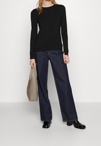 Pull noir à manches longues, jeans larges bleu foncé et bottes à talons noires. Sac à main structuré beige. Tissu lisse et design minimaliste.