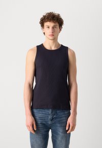 Top din bumbac negru cu textură în dungi, cu decolteu rotund, design mulat și fără mâneci, asortat cu blugi din denim ușor albastru.