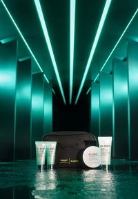 Borsa cosmetica nera contenente tre tubetti di skincare e un barattolo rotondo. I tubetti sono trasparenti con etichette verde chiaro; il barattolo ha una finitura bianca con un'etichetta.