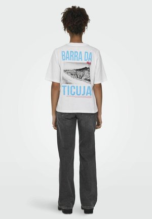 Hvid t-shirt med en sort-hvid grafik af et landskab, med "BARRA DA TICUJA" i blå og rød tekst på ryggen. Løs pasform.