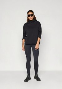 Czarna sportowa bluza z wysokim kołnierzem, długimi rękawami i bocznymi zamkami, w zestawie z czarnymi legginsami i czarnymi sportowymi butami.