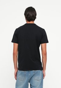 Črna bombažna majica s kratkimi rokavi in krožnim ovratnikom. Gladka tekstura. V kombinaciji z svetlo modrimi kavbojkami. Brez vidnih grafik ali vzorcev.