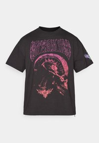 Sort bomulds t-shirt med et stort pink skull grafik og teksten "VENT FRA HELVEDE" ovenfor. Korte ærmer og en afslappet pasform.