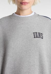 Grijze sweatshirt van zacht materiaal, met een geribbelde ronde hals, geborduurd "VANS" logo in zwart, en marineblauwe accenten op de mouwen.