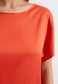 Short-sleeve top in vibrant orange, featuring a soft, smooth texture and a wide, scoop neckline. Minimal seams and simple design.