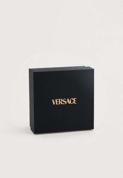 Μαύρο ορθογώνιο κουτί με τη λέξη "VERSACE" σε χρυσά κεφαλαία γράμματα στο κέντρο της μπροστινής πλευράς, πάνω σε απλό λευκό φόντο.