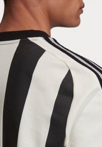 Sort og hvid sportstrøje med ribbet halsudskæring og sorte striber på skuldrene, der har struktureret stof og en tætsiddende design.