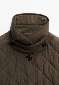 Quiltet brun jakke med høj krave, sorte knapper og en glat, let skinnende tekstur med diagonal mønster.