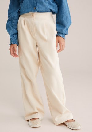 Pantalon ample couleur crème avec tissu texturé, présentant un pli avant et une fermeture à bouton à la taille. Stylé avec une chemise en denim.