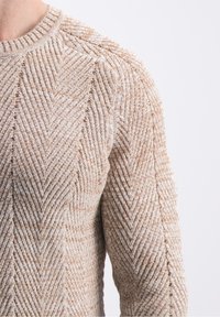 Hellbrauner gestrickter Pullover mit Fischgrätmuster, gerippter Halslinie und strukturierter Oberfläche mit ineinandergreifenden Fäden für mehr Tiefe.