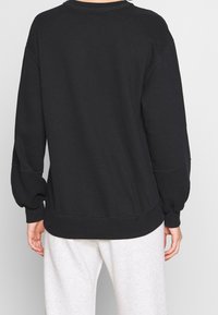 Sudadera negra con corte relajado, mangas de globo y puños acanalados. Presenta costuras visibles y un dobladillo curvado.