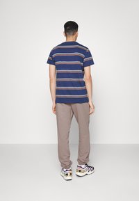 Marinblå randig t-shirt med kort ärm, kombinerad med ljusbruna joggingshortser och flerfärgade sportskor, sedd bakifrån.