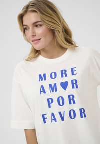 Biała bawełniana koszulka z krótkim rękawem, z wyraźnym niebieskim napisem "MORE AMOR ♥ POR FAVOR". Klasyczny okrągły dekolt.