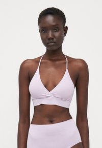 Bralette violet clair avec un décolleté en V, des fines bretelles et un design avant torsadé. Texture lisse et style minimaliste, associé à un bas assorti.