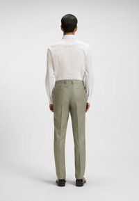 Biała koszula z długim rękawem o gładkiej fakturze, z mankietami z podwójnymi guzikami, w połączeniu z jasnoszarymi spodniami w kant o delikatnym wzorze.