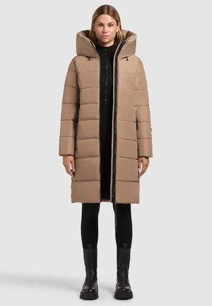 Lang, lichtbruine pufferjas met een hoge kraag en ritssluiting, voorzien van gestikte secties en zijzakken. Draag het over een zwarte outfit.