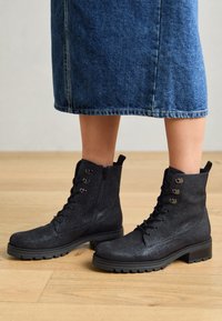 Bottes noires à la cheville en matériau texturé, avec un laçage à l'avant, une fermeture éclair sur le côté, et une semelle en caoutchouc au design épais et aux œillets métalliques.
