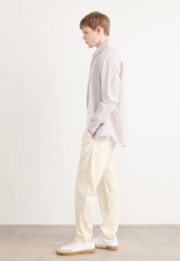 Camisa de manga larga a rayas en rosa claro y blanco, combinada con pantalones relajados en blanco roto y zapatillas blancas con suelas de goma.