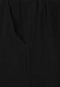 Svart plagg med en texturerad yta, med en avslappnad design. Tyget har en mjuk känsla och ett subtilt, rynkat mönster.