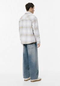 Flannel shirt in light blue and beige plaid, paired with loose-fitting faded blue denim jeans and off-white sneakers.