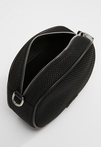 Zwarte mesh schoudertas met een ronde vorm, zilveren ritssluiting en leren accenten. Heeft een metalen lus aan de zijkant.