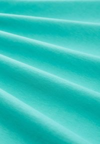 Turquoise katoen stof met een gladde textuur, met een serie van zachte, vloeiende plooien en een constante kleur zonder patronen.