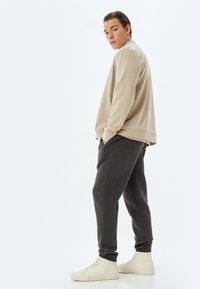 Beige sweatshirt, donkergrijze joggers en off-white sneakers. Zachte stof, relaxte pasvorm, elastische boorden op de broek, zijzakken. Minimalistisch ontwerp.