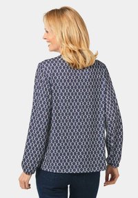 Marineblaues Hemd mit weißem geometrischen Muster, langen Ärmeln, lässiger Passform und abgerundetem Saum. Material aus Baumwollmischung mit weicher Textur.