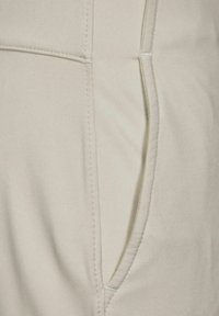 Ljust beige byxor med en slät yta, förstärkta sömmar vid sömmarna samt en sidoficka med en diskret vinklad öppning.