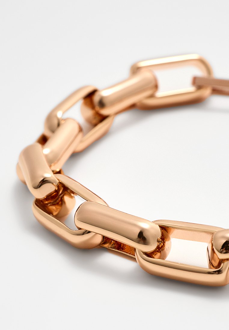 Detailaufnahme von glänzenden roségoldenen rechteckigen Gliederketten, die zu einem Armband auf einer weißen Oberfläche angeordnet sind.
