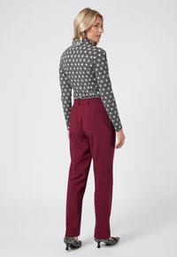 Top a righe bianche e nere abbinato a pantaloni bordeaux. Il top ha maniche lunghe e un design aderente, mentre i pantaloni hanno una vestibilità dritta.