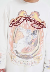 Witte shirt met een ontwerp van een skeletcowboy die op een oprijzende witte paard rijdt, met vlammen, hoefijzers en de teksten "Ed Hardy" en "Dead or Alive."